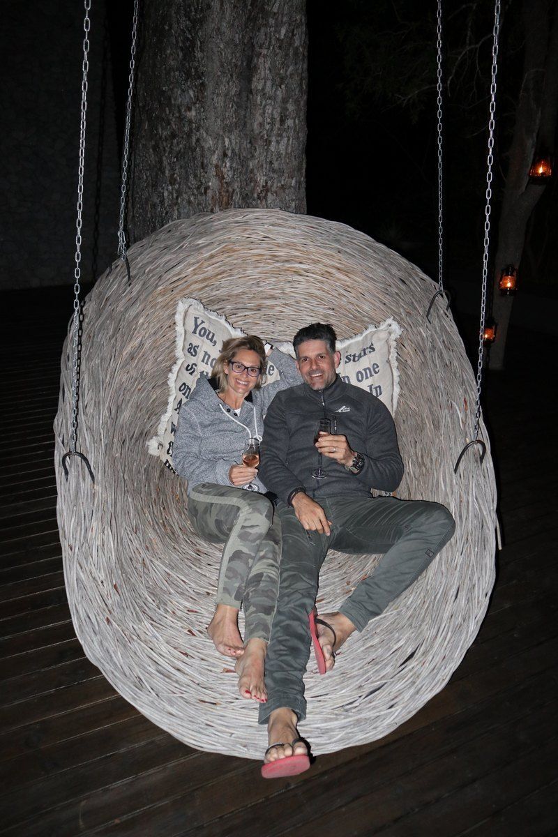 Couple sits in a large, woven swing outdoors at night, smiling.