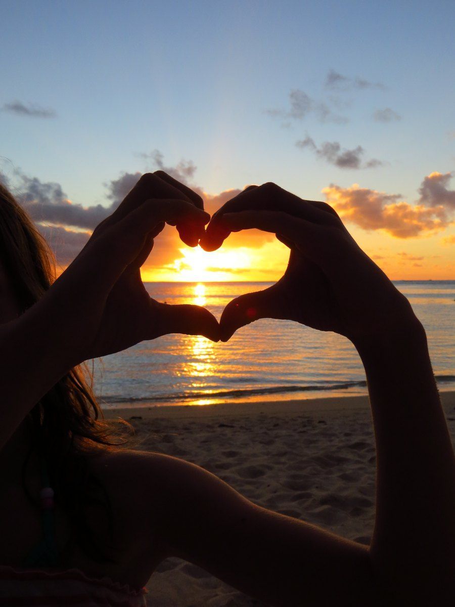 Hands forming a heart around a sunset over the ocean.