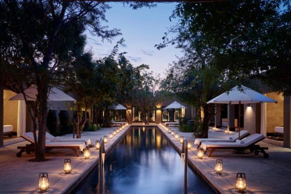 Long, narrow pool at dusk, with white lounge chairs, cabanas, and lanterns lining the sides.