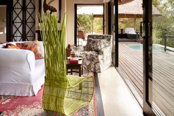 Cozy living area opens to a deck. A wicker chair with a green plant sits on a rug near a couch and a patterned armchair.