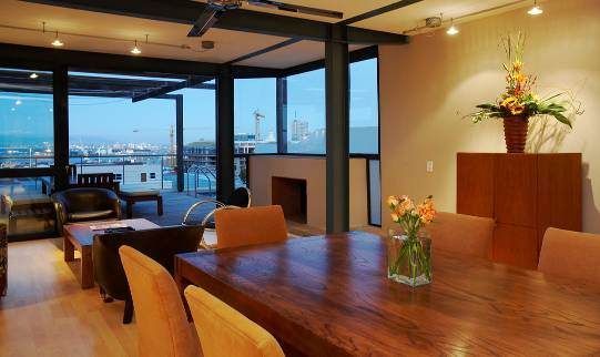 A modern, well-lit dining room with a large wooden table and city views through expansive windows.