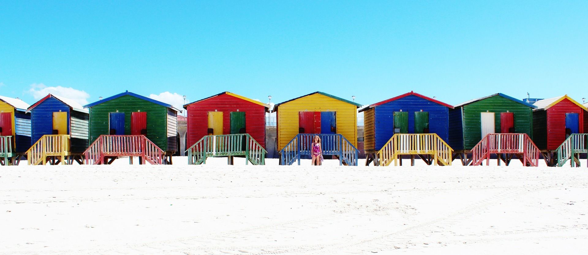 Colorful beach huts on a sandy beach under a clear blue sky.