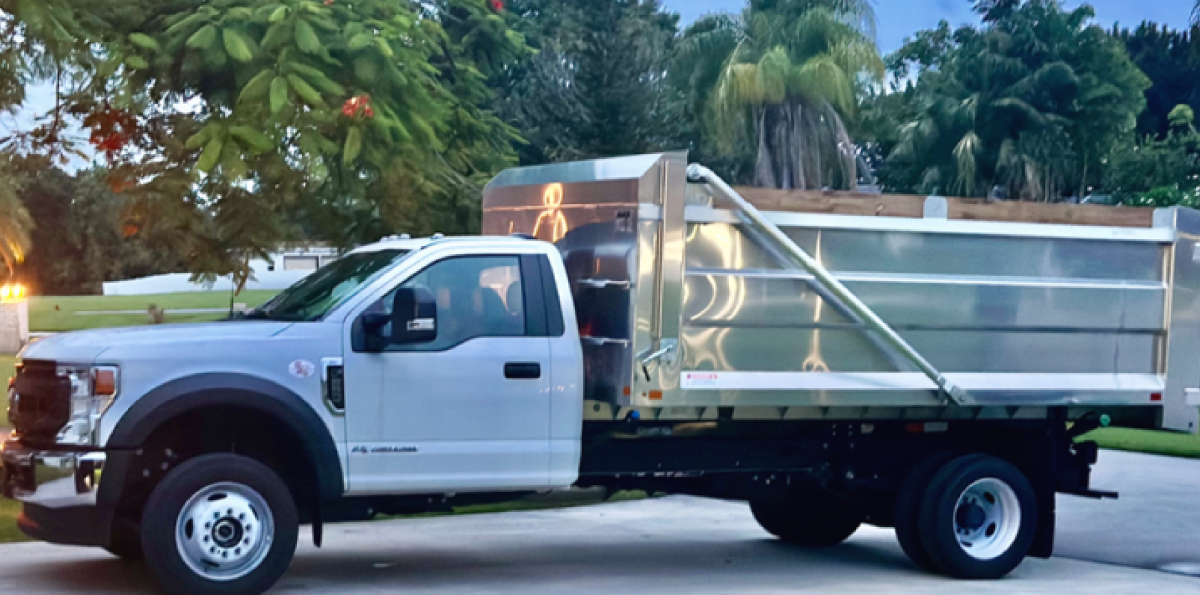 White dump truck parked on a street beside palm trees, side view