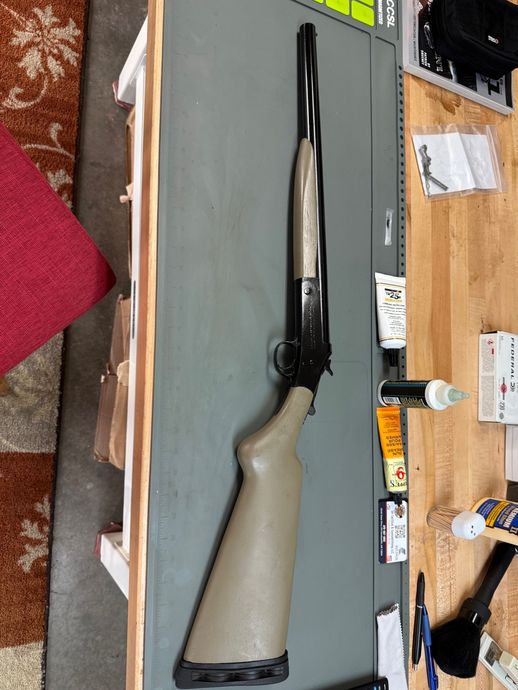 Black and gray shotgun laying on a workbench with wooden cabinets and small tools nearby