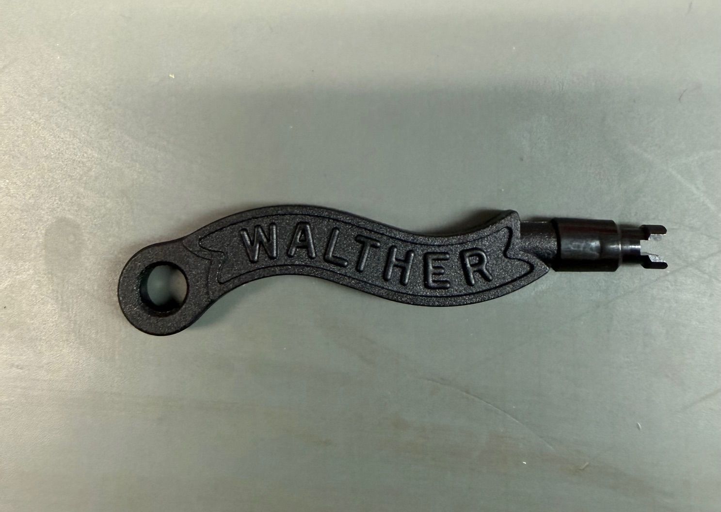 Black metal Wallace tool with a key-ring hole and pointed double-prong end on a light background
