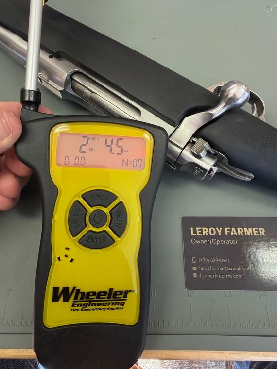 Handheld digital gauge measuring a clamp near a Leroy Farmer tool card, with a reading of 24.5.