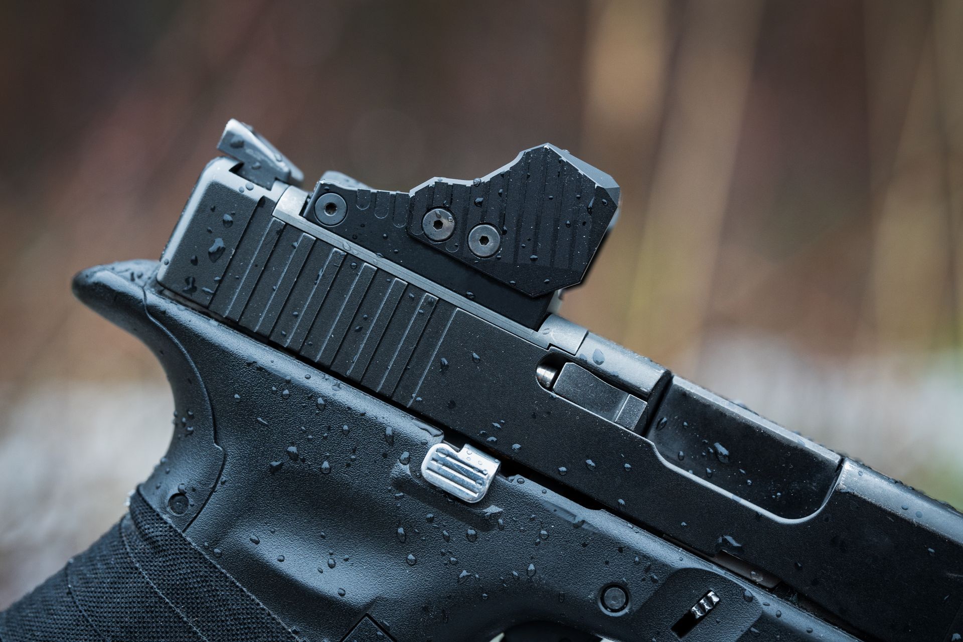 Black handgun with red-dot sight and raindrops on a wet surface