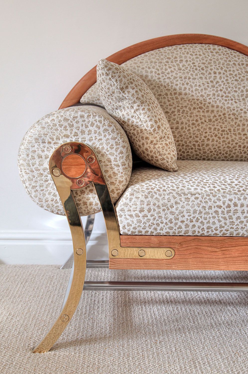 A close up of a custom made sofawith a leopard print fabric and a brass arm.