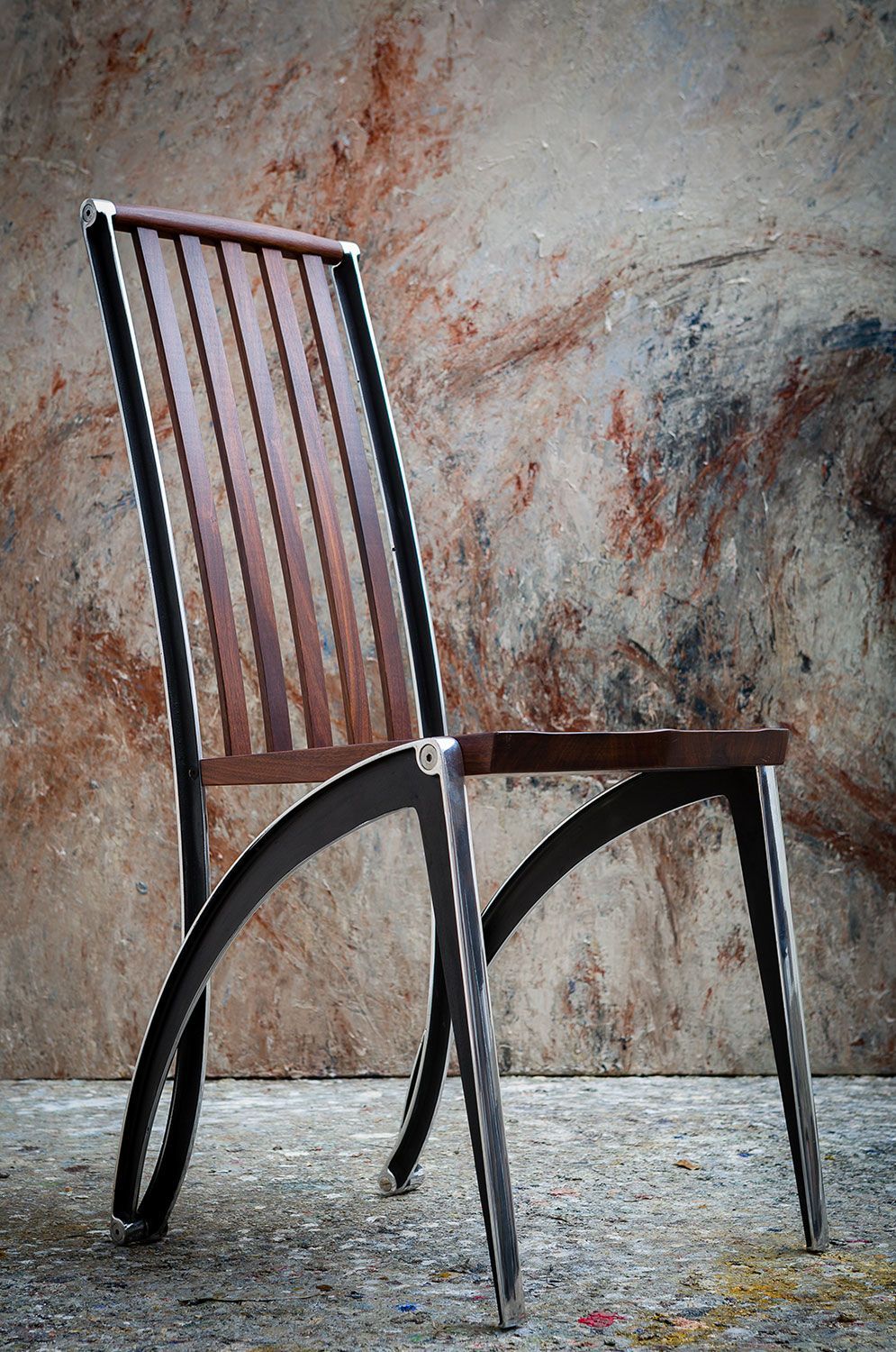 A handcrafted walnut chair with metal legs is sitting in front of a wall.