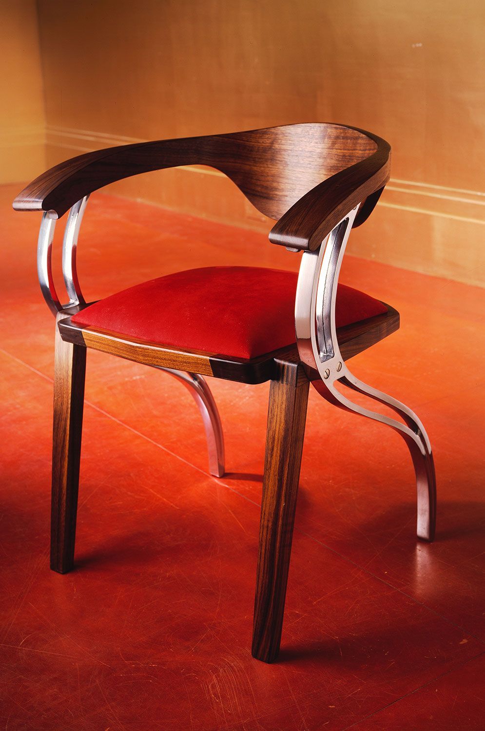 A unique designer wooden chair with a red cushion sits on a red floor