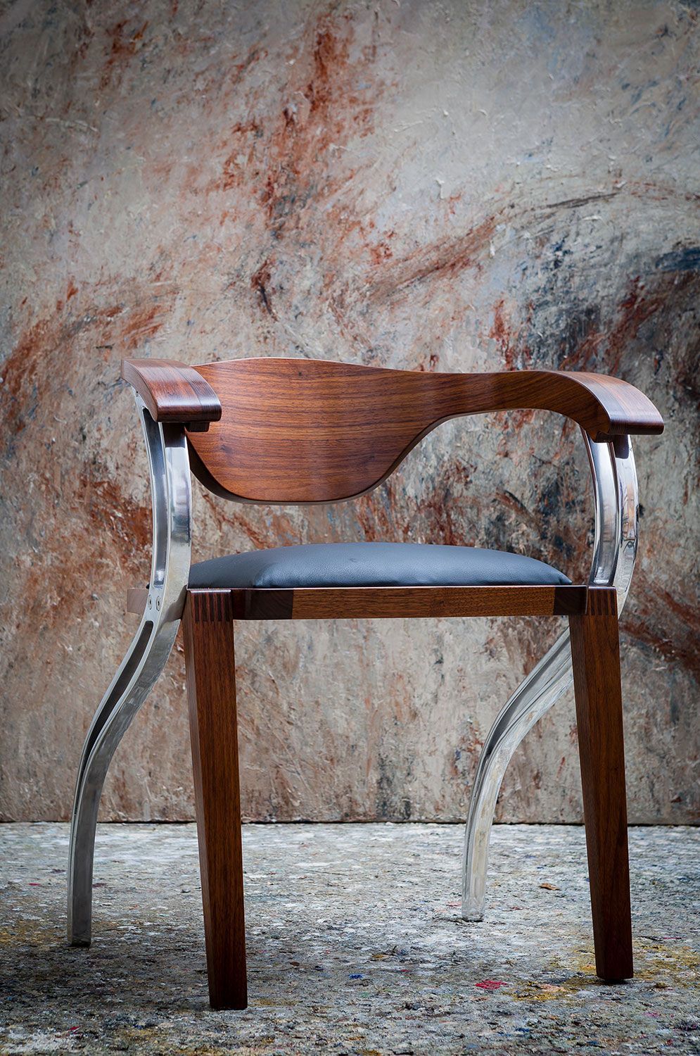 A wooden chair with metal legs is sitting in front of a wall.