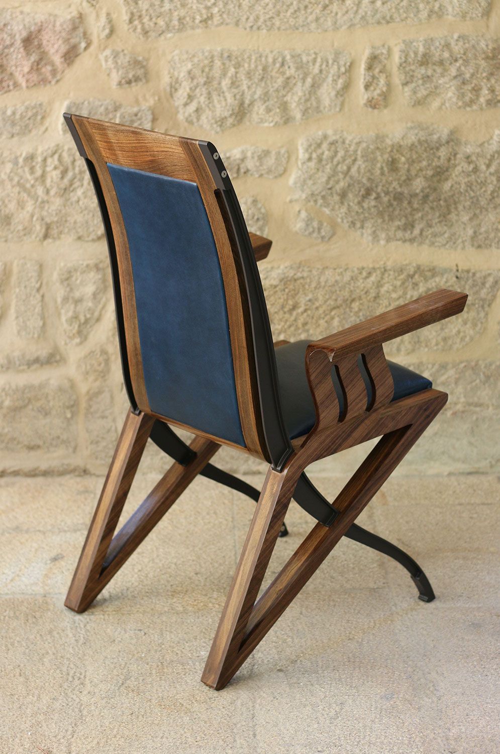 A highendwooden chair with a blue leather cushion is sitting in front of a stone wall