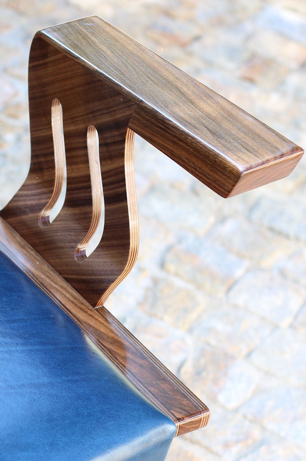 A close up of a Custom build wooden chair arm rest on a brick floor.