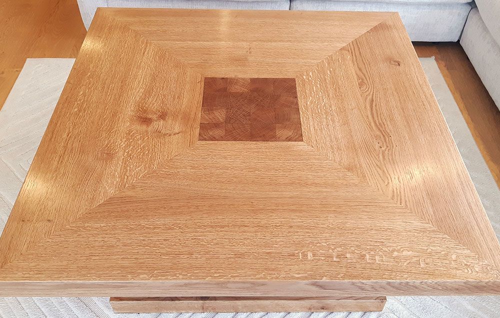 A custom made oak coffee table is sitting on top of a white rug in a living room.