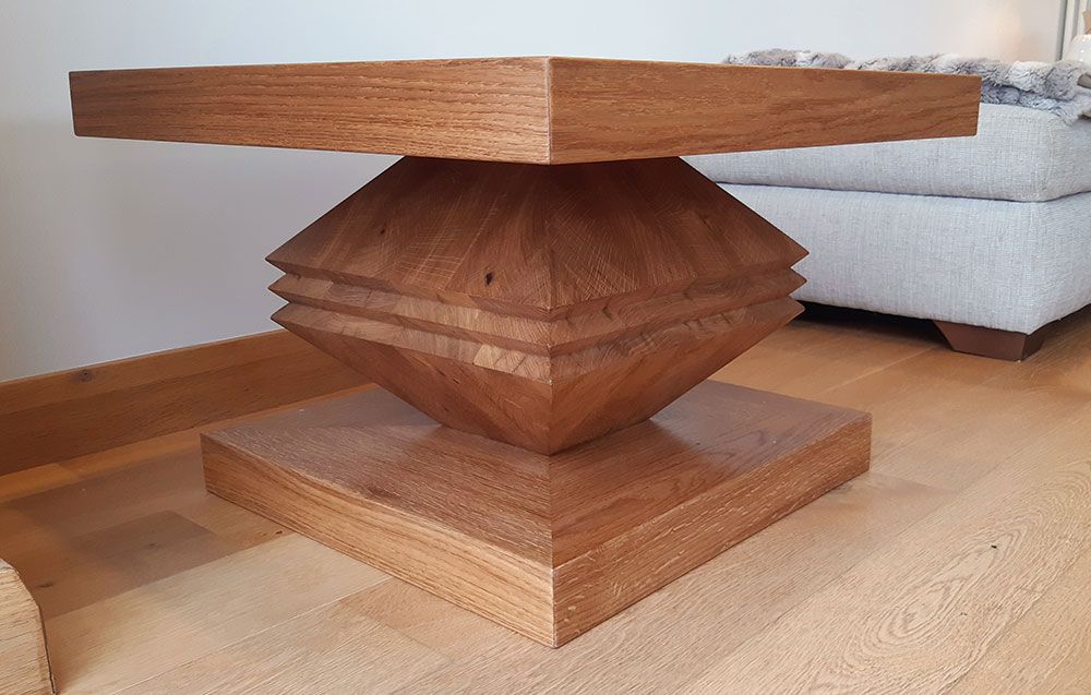 A handcrafted oak wooden coffee table is sitting on a wooden floor next to a couch.