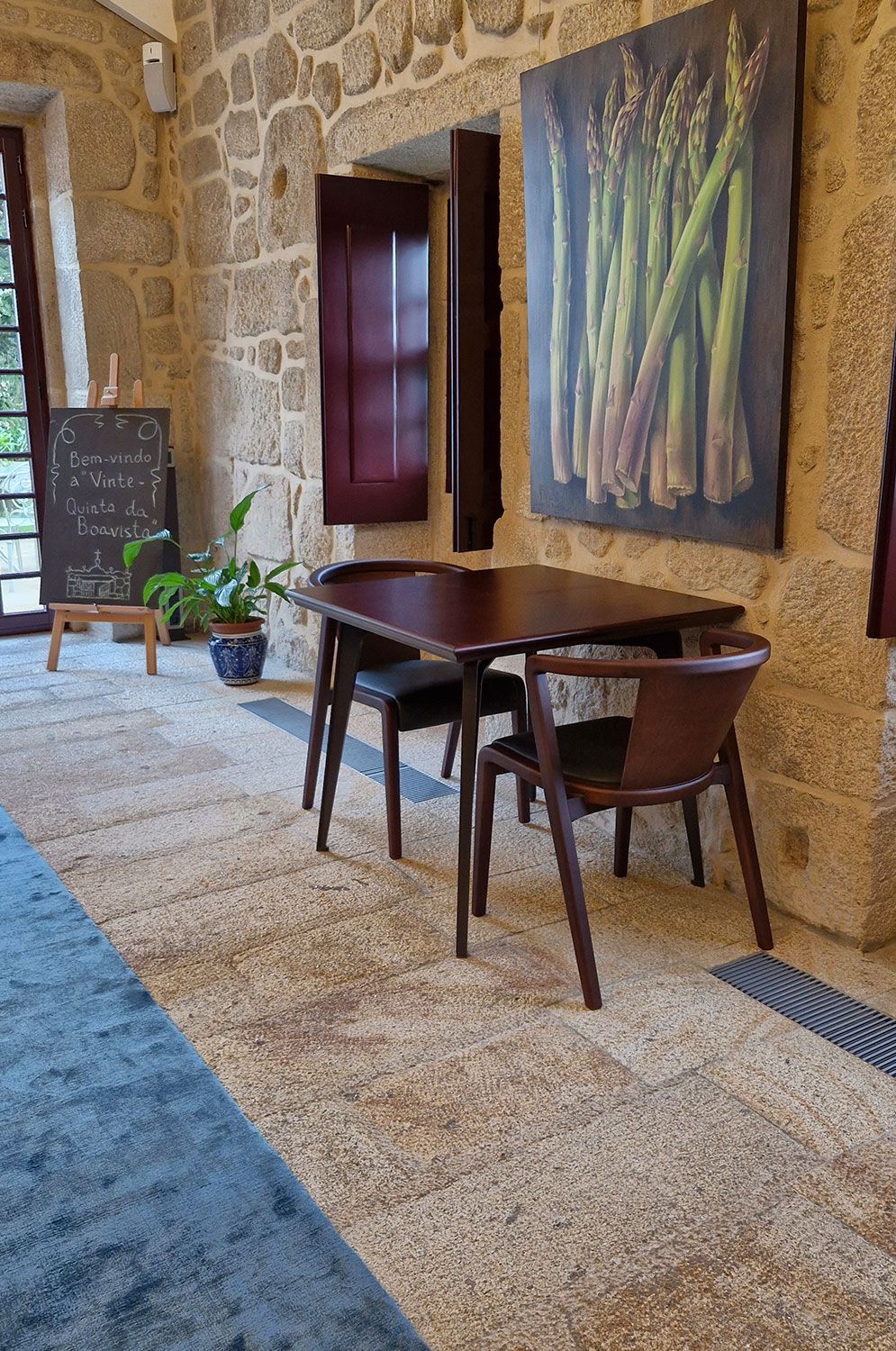 Handcrafted table and chairs in a café with a painting of asparagus on the wall.