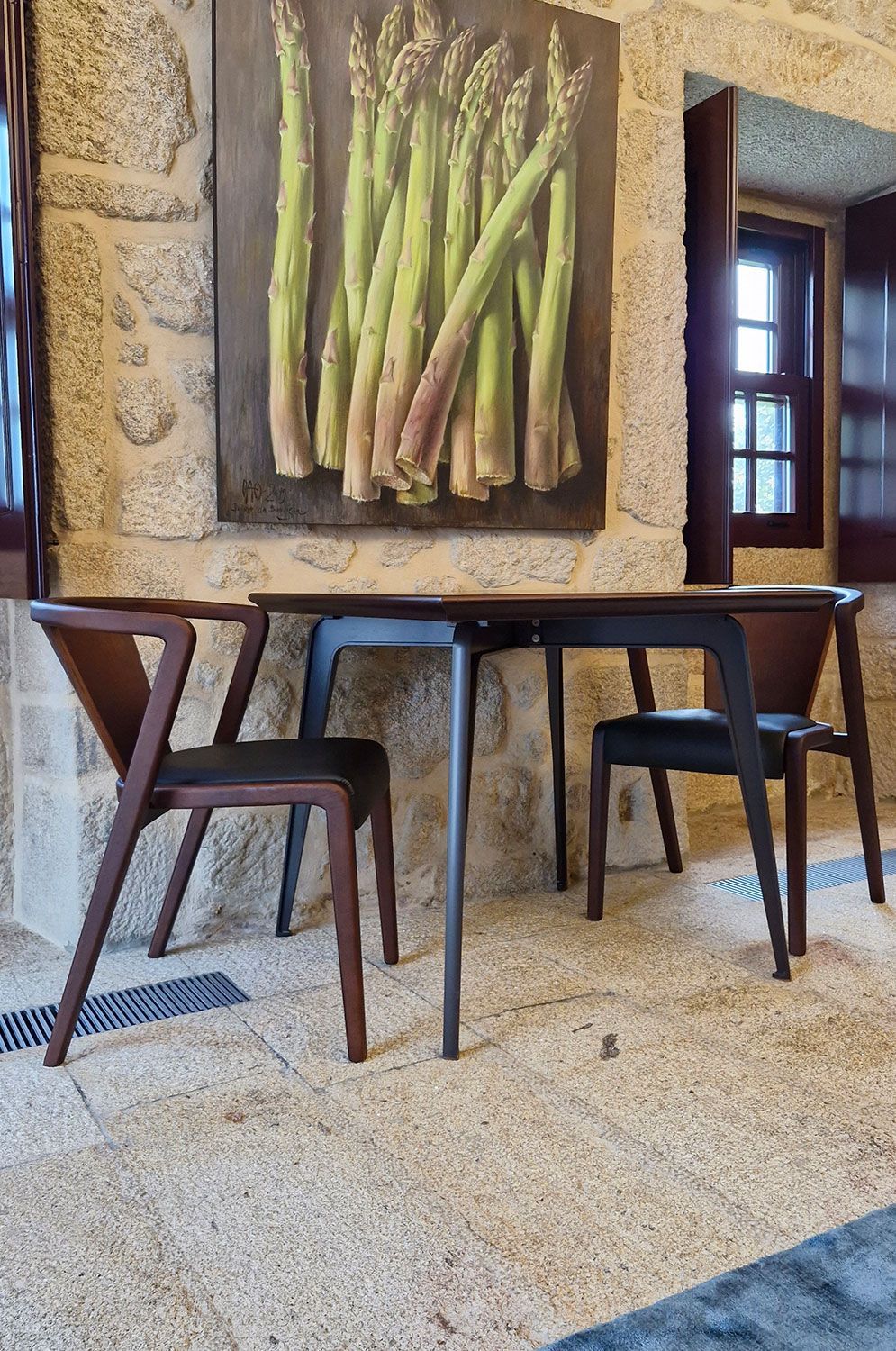 A table and chairs for a cafe with a painting of asparagus on the wall.