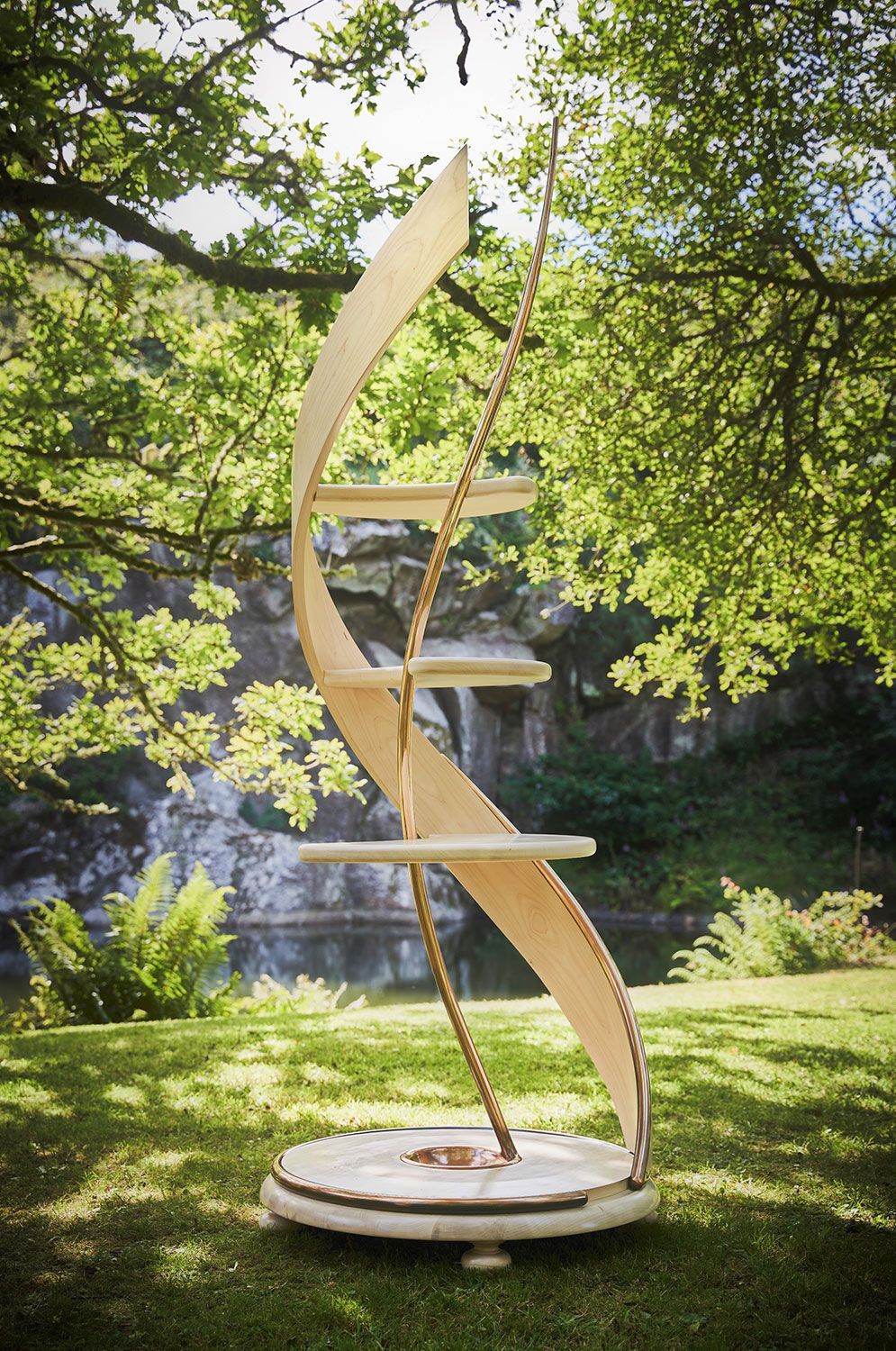 A wooden designer sculpture in the shape of a dna is sitting on top of a lush green field.