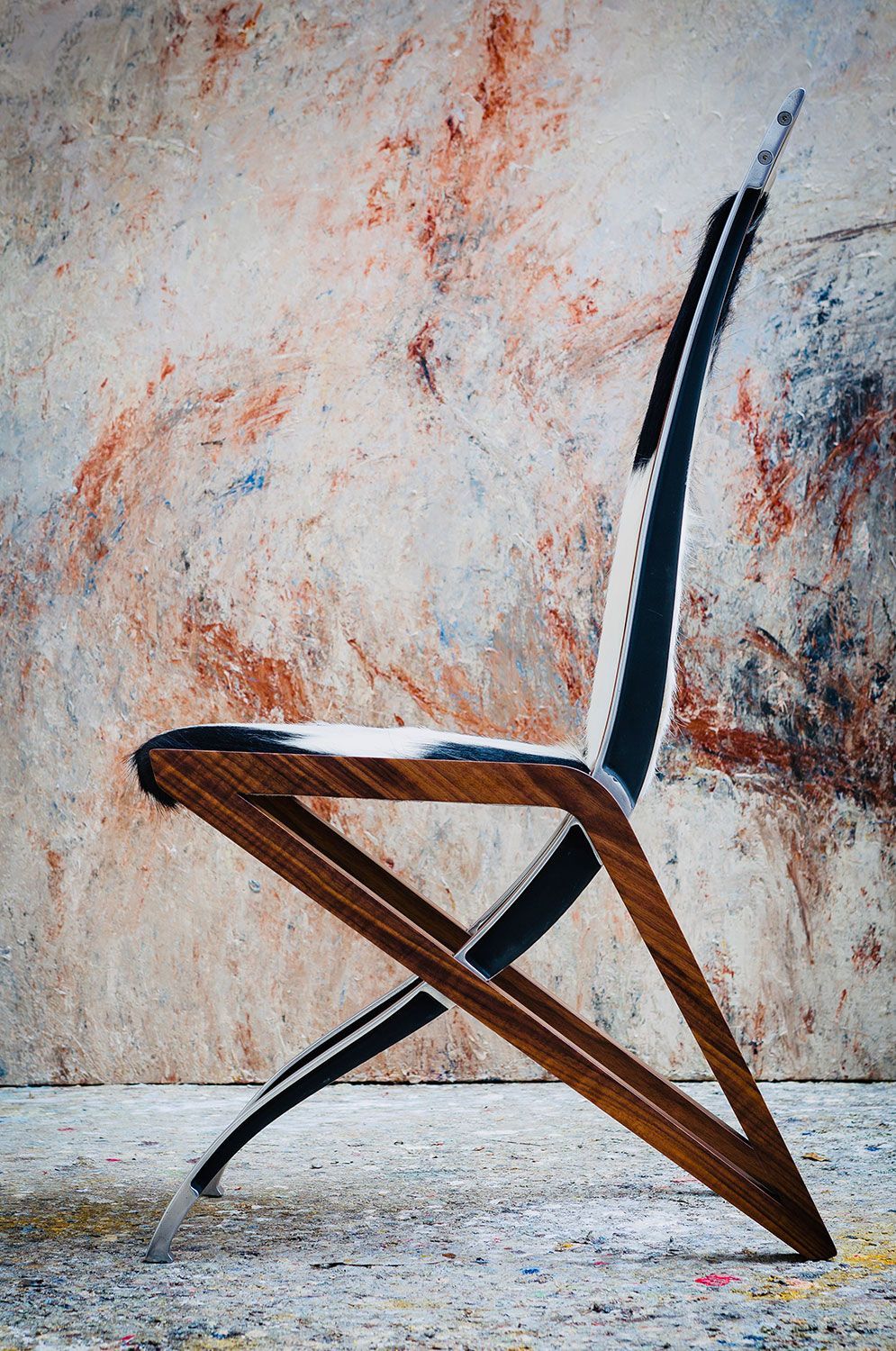 A wooden chair with a cowhide seat is sitting in front of a wall handcrafted by a furniture desinger