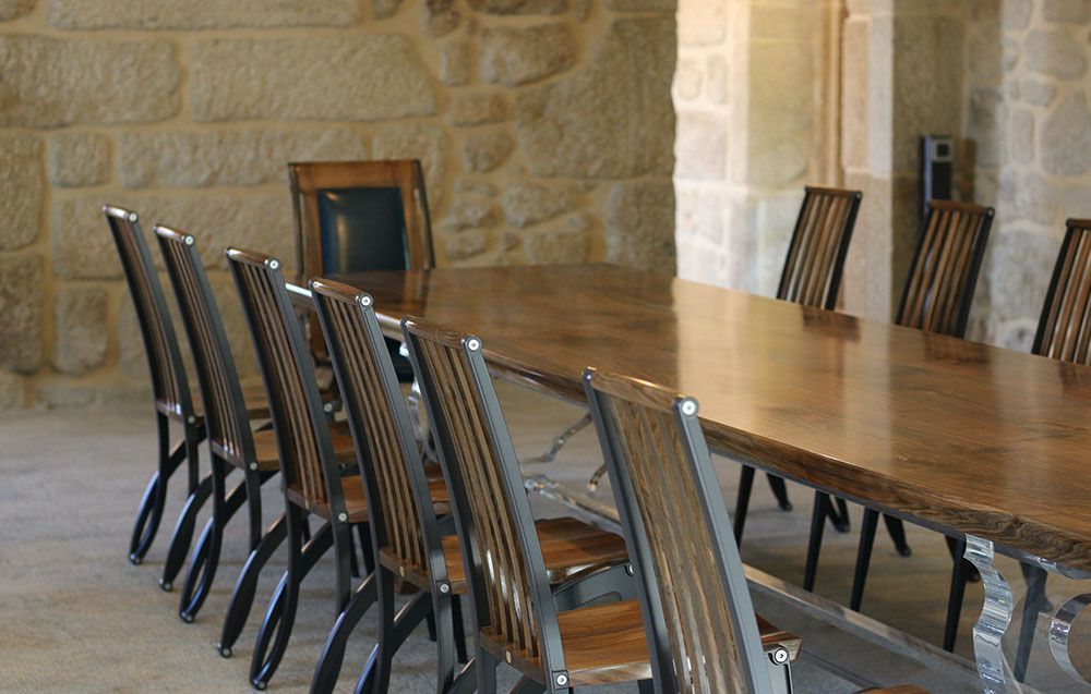 A long tailor made walnut table with chairs in front of a stone wall