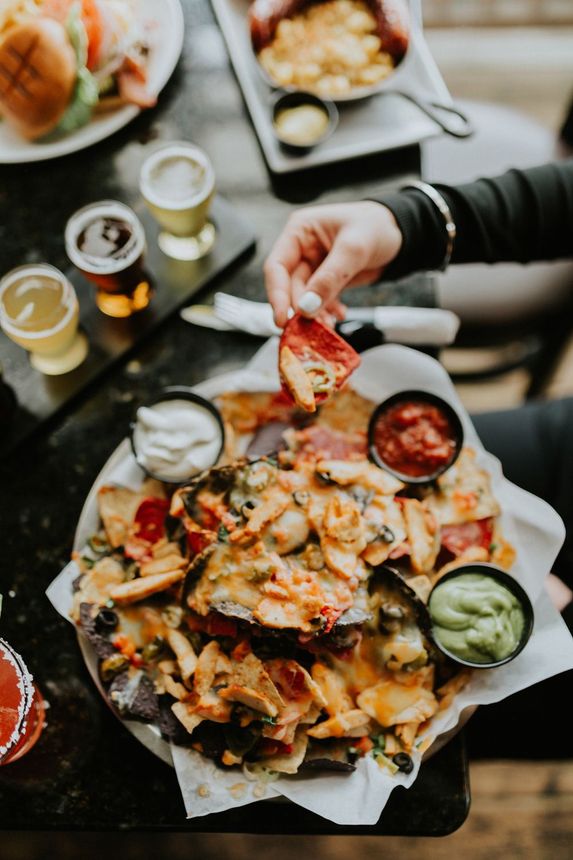 A person is dipping a tortilla chip into a bowl of nachos.