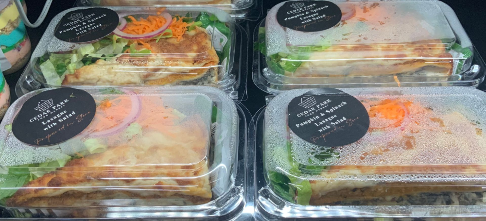 Packaged salad meal containers with greens, carrots, and labels on a shelf— Cedar Park Supermarket In Taranganba, QLD