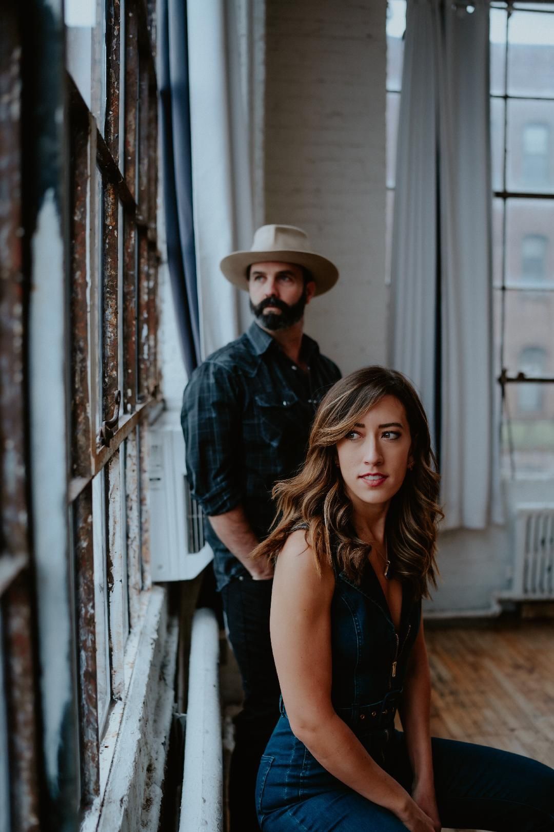 A man and a woman are standing next to each other in front of a window.