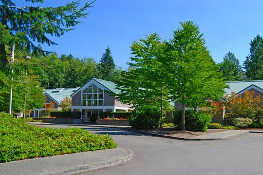 A large building with a green roof is surrounded by trees and bushes.