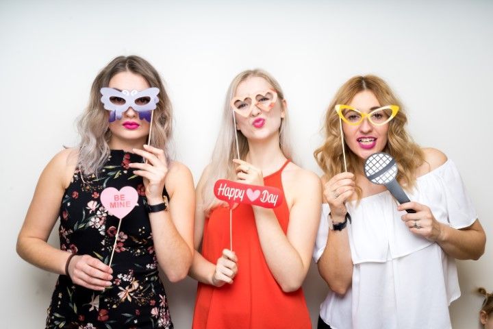 Three women posing with playful signs and novelty sunglasses against a white background