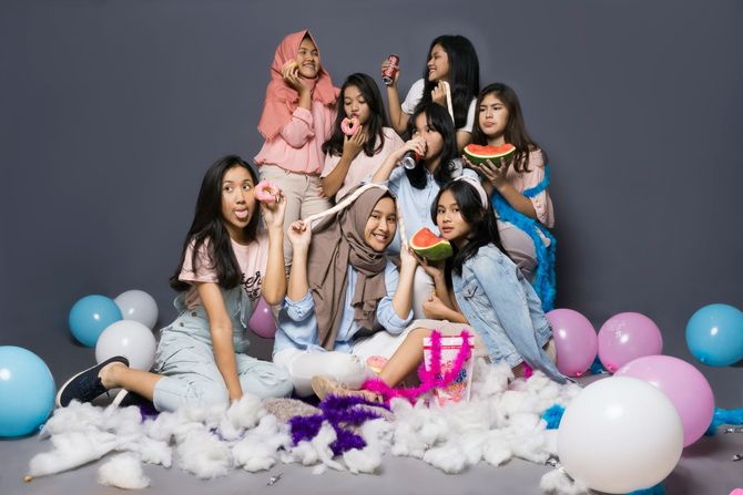 Group posing on a gray studio floor with pastel balloons and white fluffy props, smiling and playful