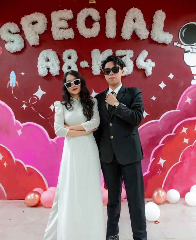 Two people posing in formal wear in front of a pink “Special 8” celebration backdrop.