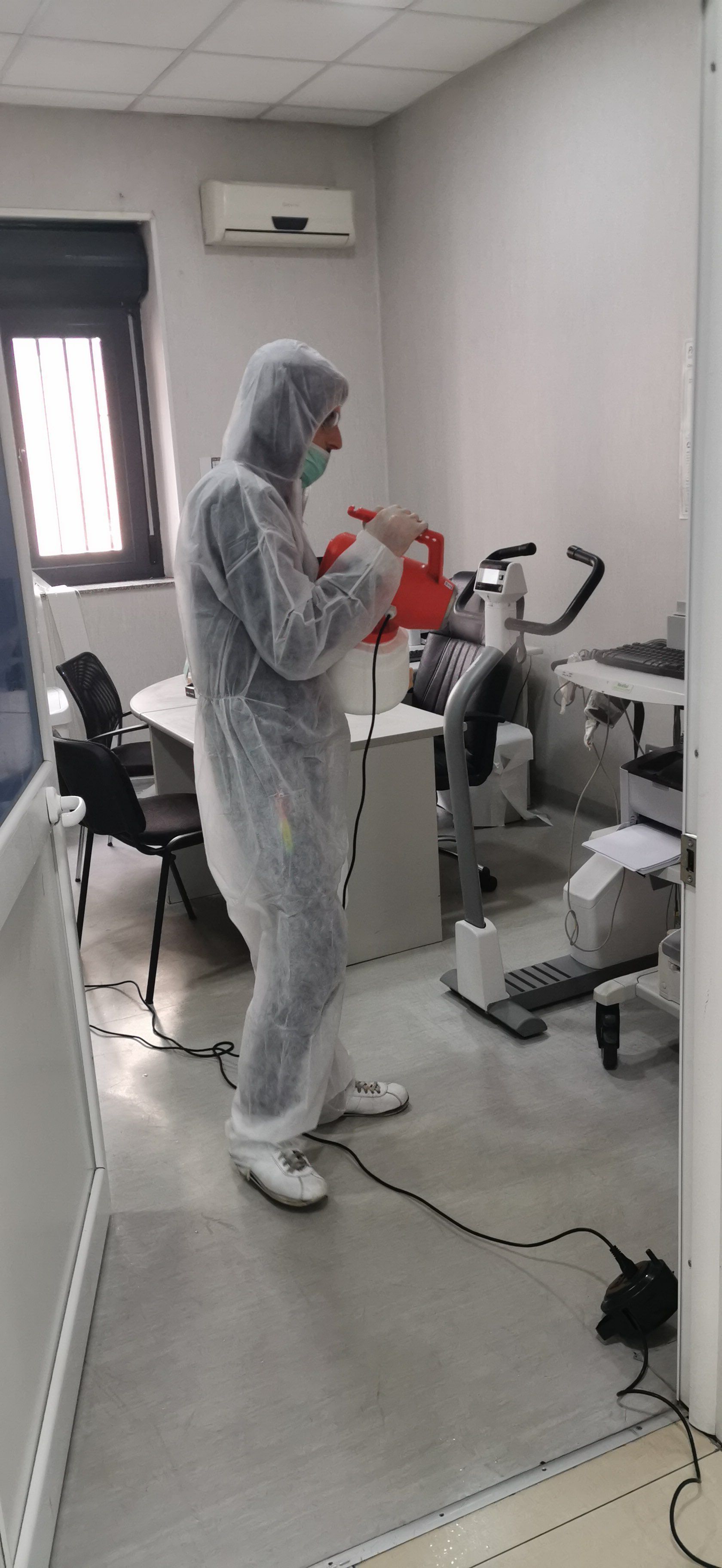 Persona con tuta protettiva che disinfetta uno studio medico con attrezzi ginnici.