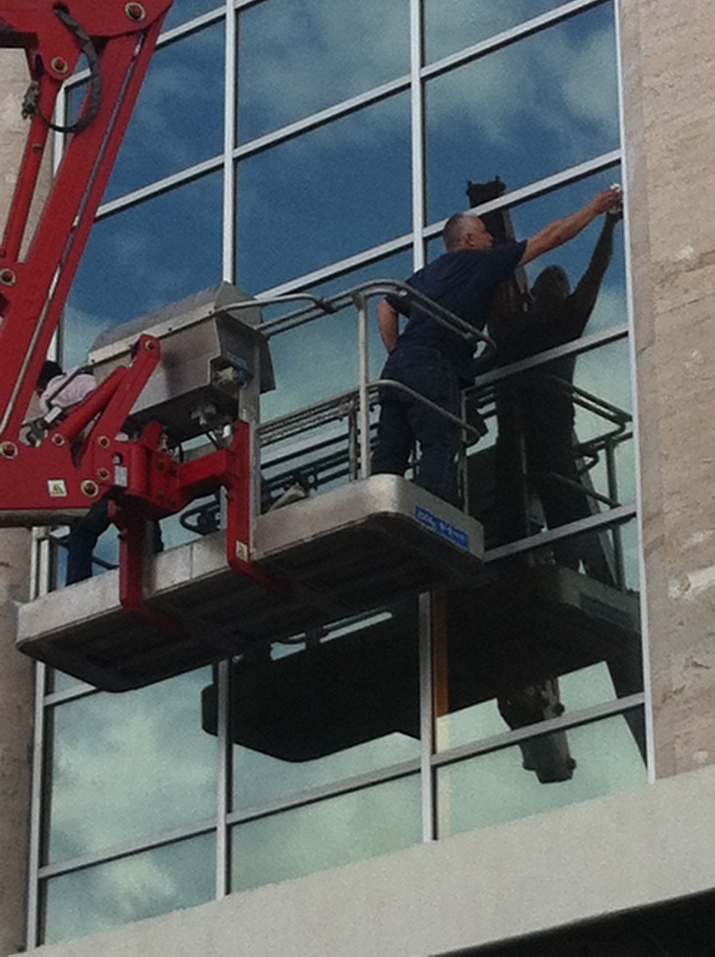 Due operai puliscono una grande finestra di un edificio utilizzando una piattaforma aerea.