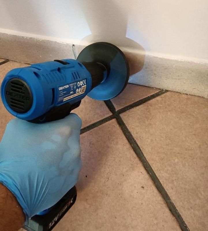 Una persona con un guanto blu tiene in mano una piastrella per levigatura blu e nera vicino a un muro bianco.