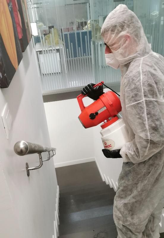 Persona con tuta protettiva che disinfetta il corrimano delle scale con uno spruzzatore.