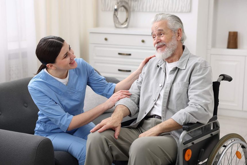 Caregiver comforting seated patient in a wheelchair in a bright living room