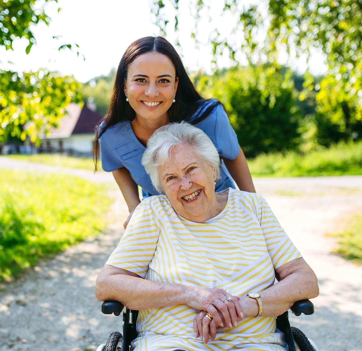 Woman pushing smiling elderly person in wheelchair on a sunny path outdoors
