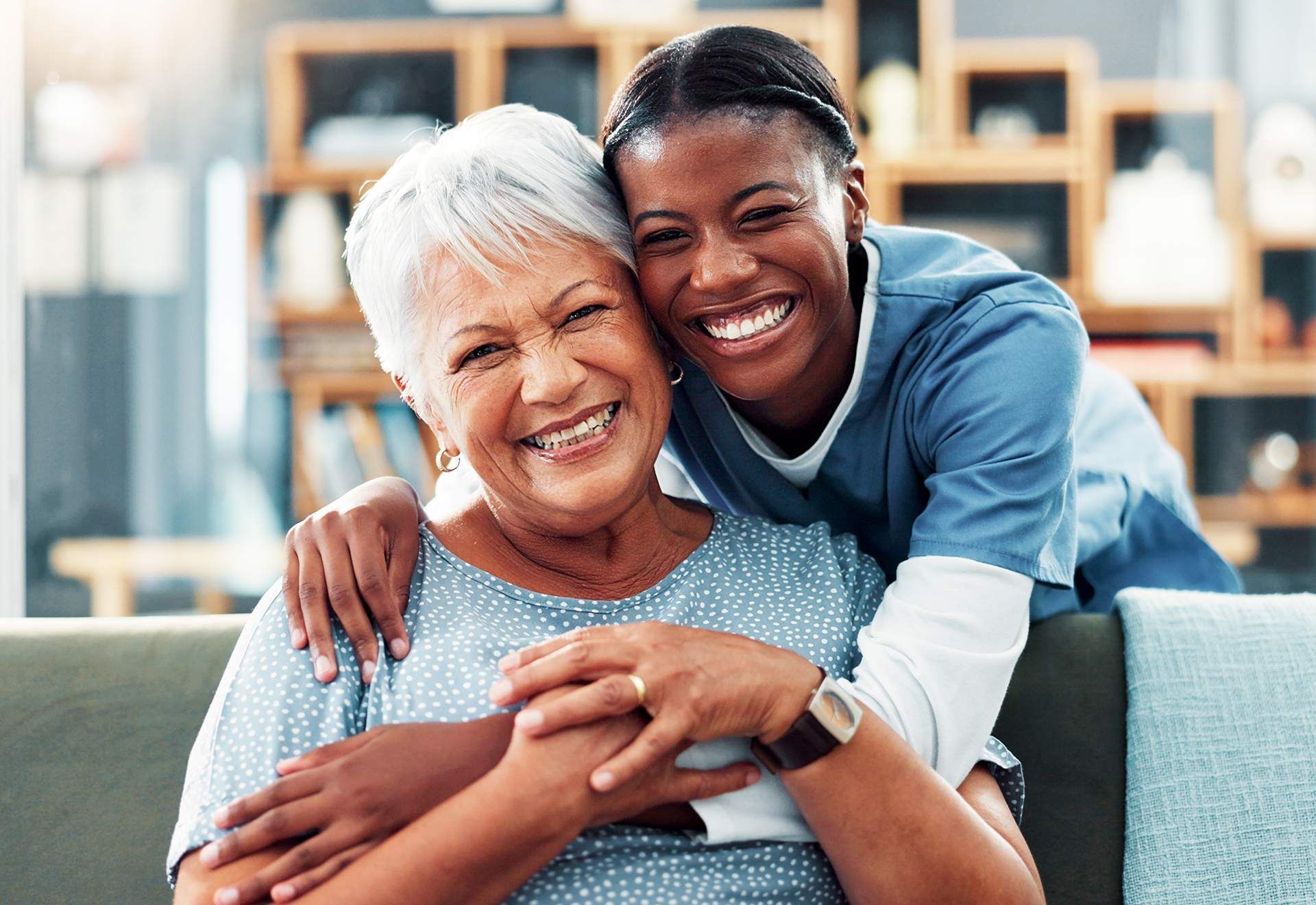 Two smiling people hugging on a couch in a bright living room