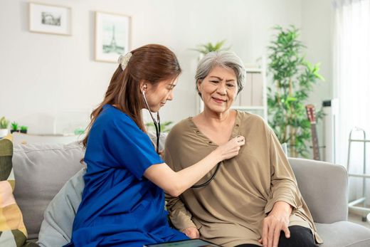 Caregiver adjusting clothing on smiling older woman seated on a couch in a bright living room