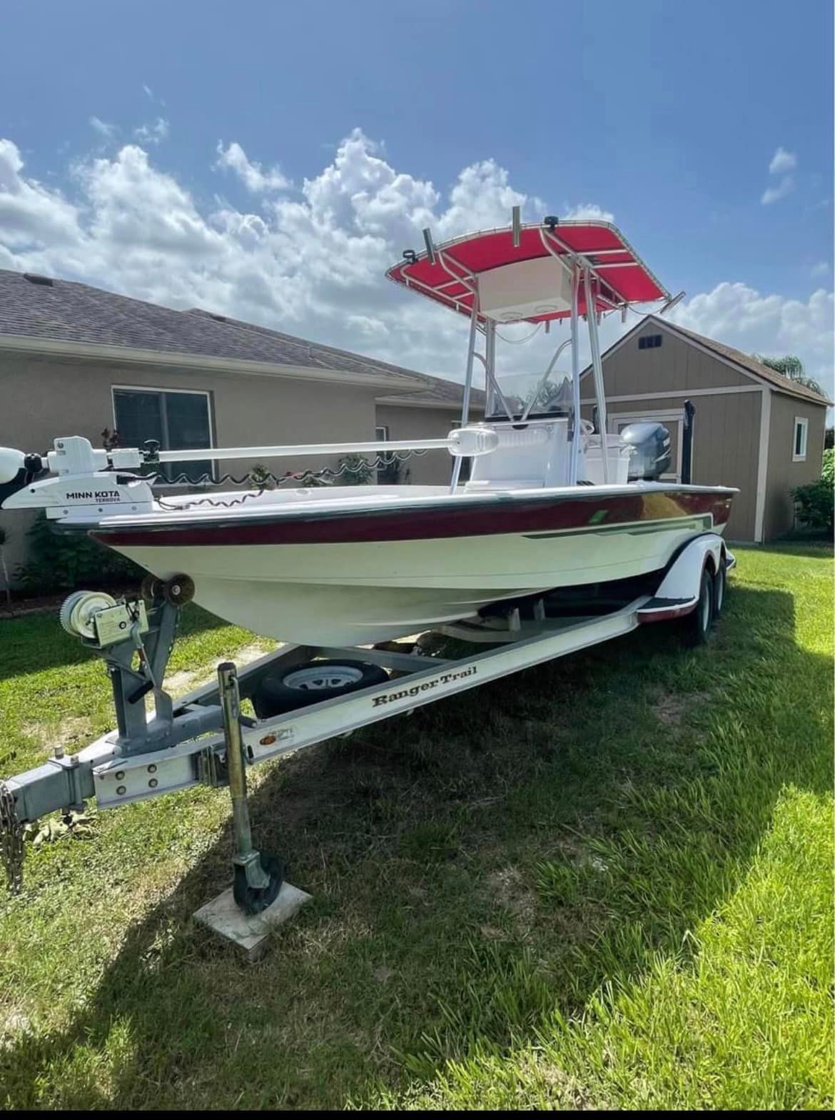 A white and red fishing boat on a trailer, under a blue sky, on a lawn.