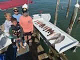 People on a dock with a large catch of fish laid out on a table.