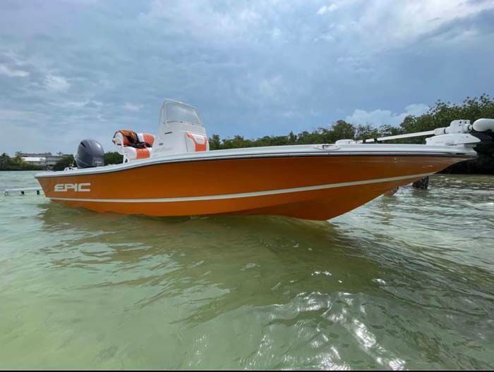 Orange and white boat on water with a cloudy sky and mangroves in the background.