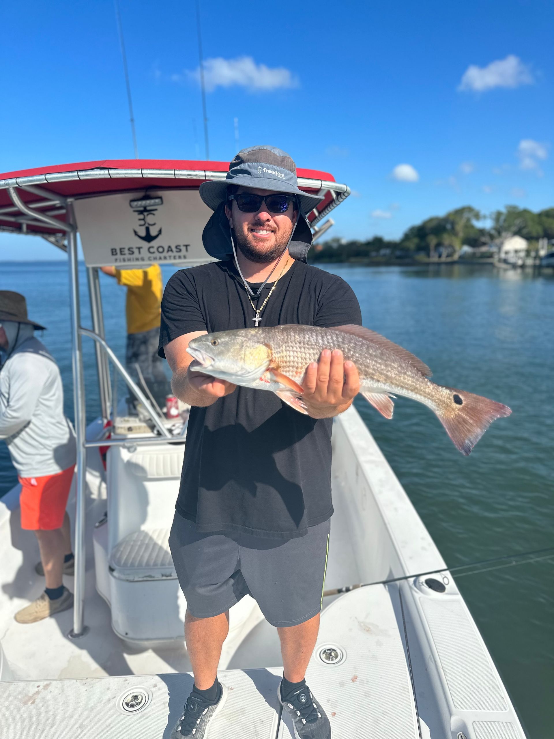 Man on boat holding up a large redfish. Sunny day, coastal setting.