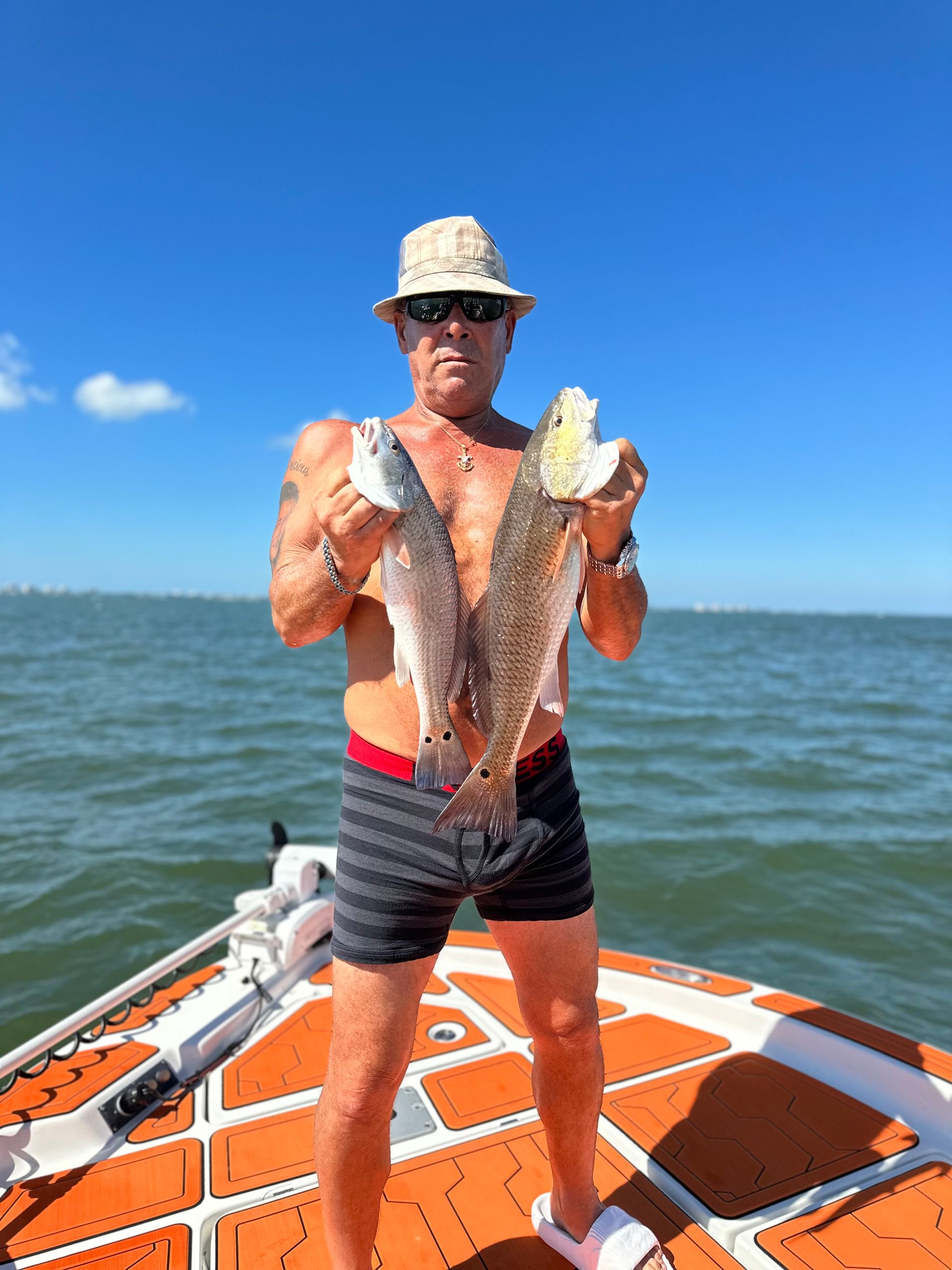 Man holding two fish on a boat in sunny weather.