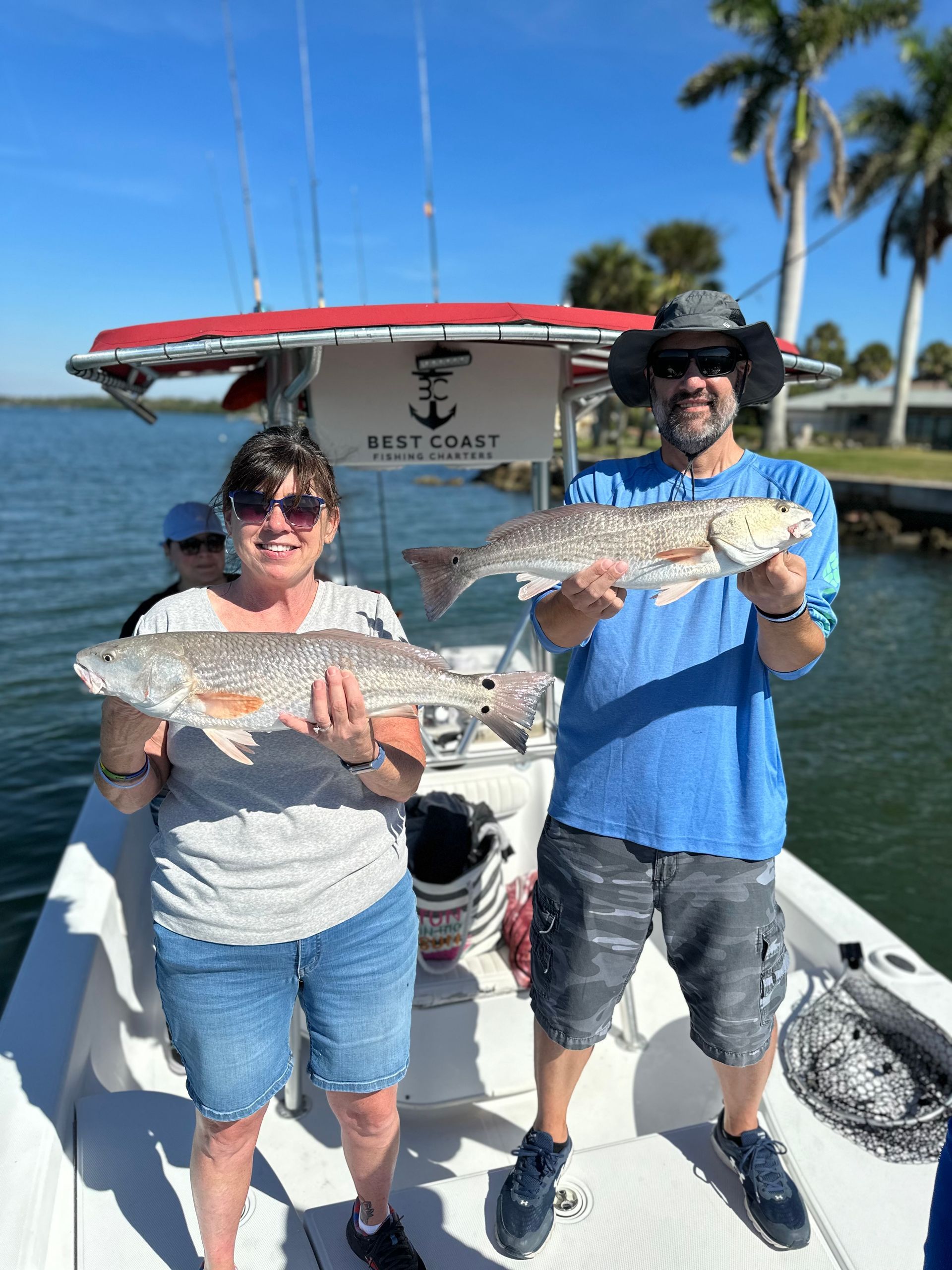 Two people on a boat holding large fish they caught, sunny day.
