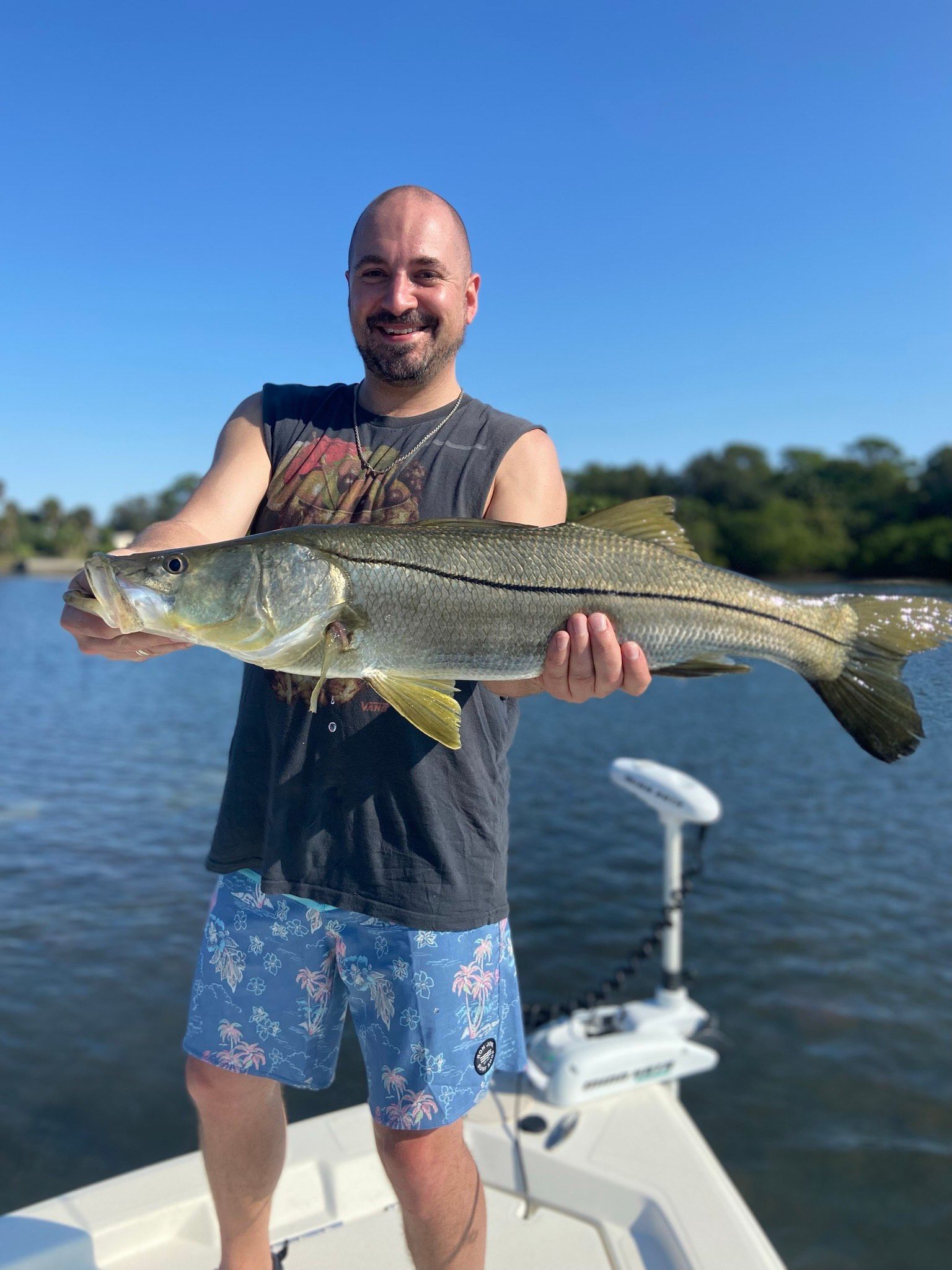 Man holding a large snook fish on a boat, blue water and sky in background.