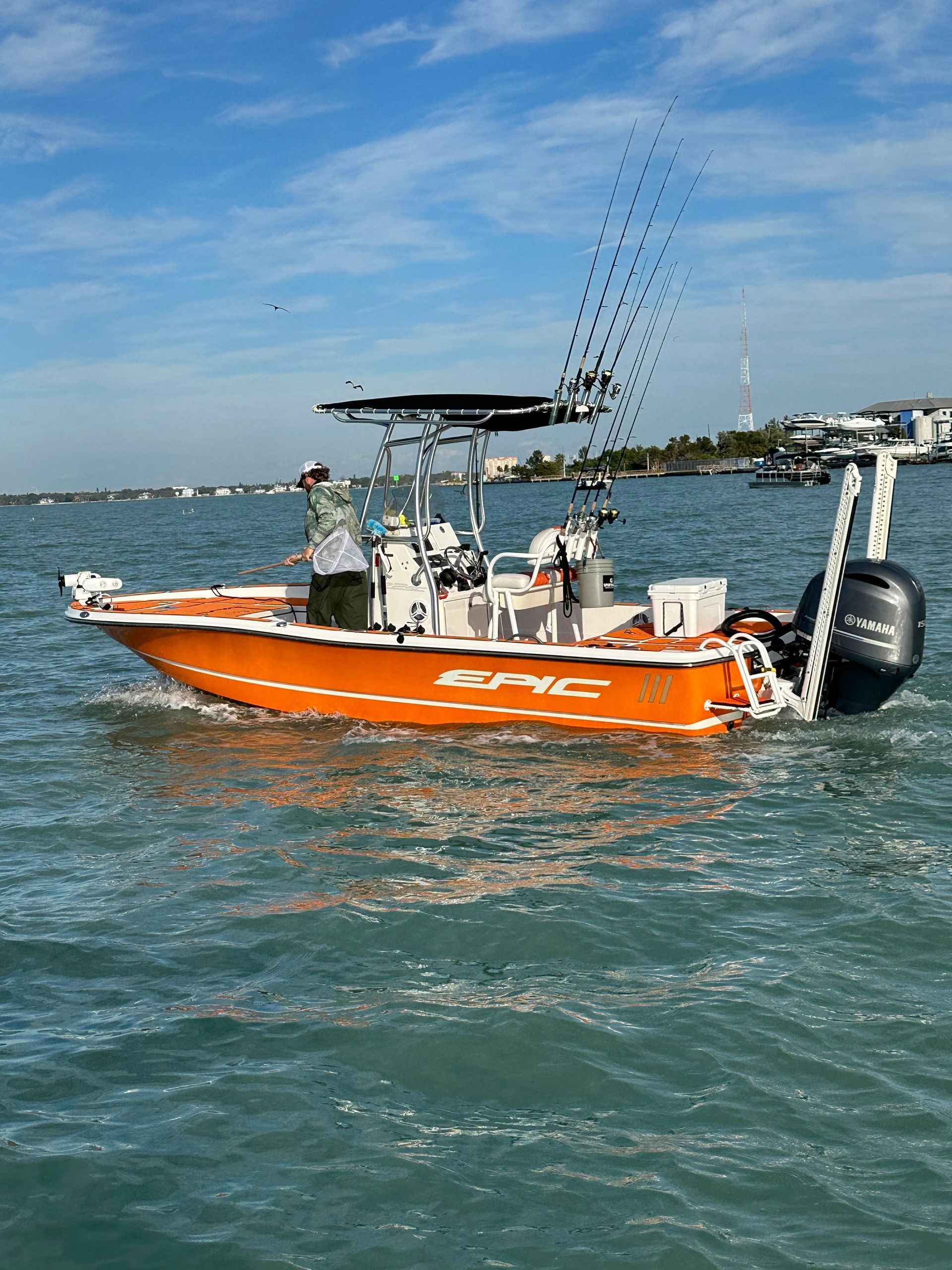 Orange fishing boat on water with blue sky and shoreline in background.
