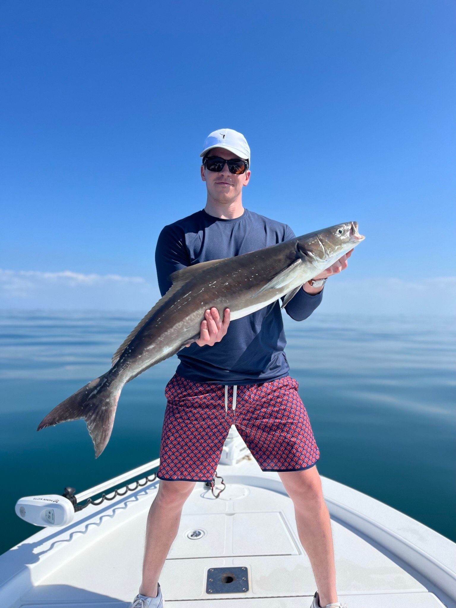 Man holding a large fish on a boat, blue sky and water.