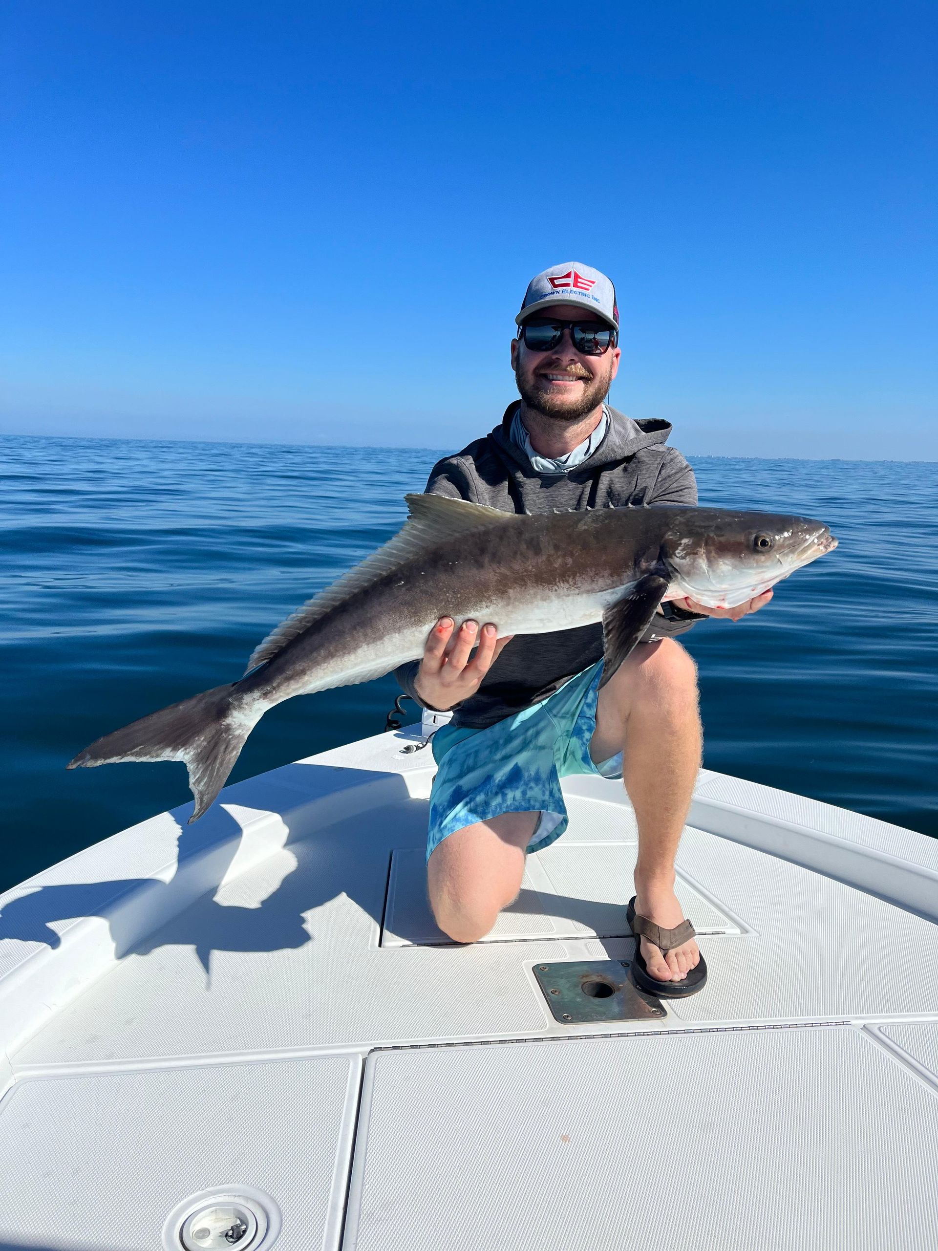 Man kneeling on boat holding large fish against ocean backdrop.