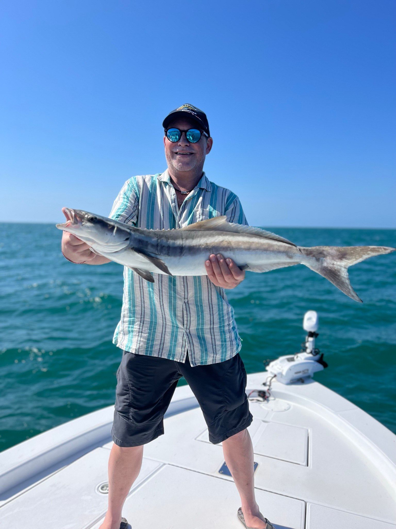 Man holding a fish on a boat in sunny weather.